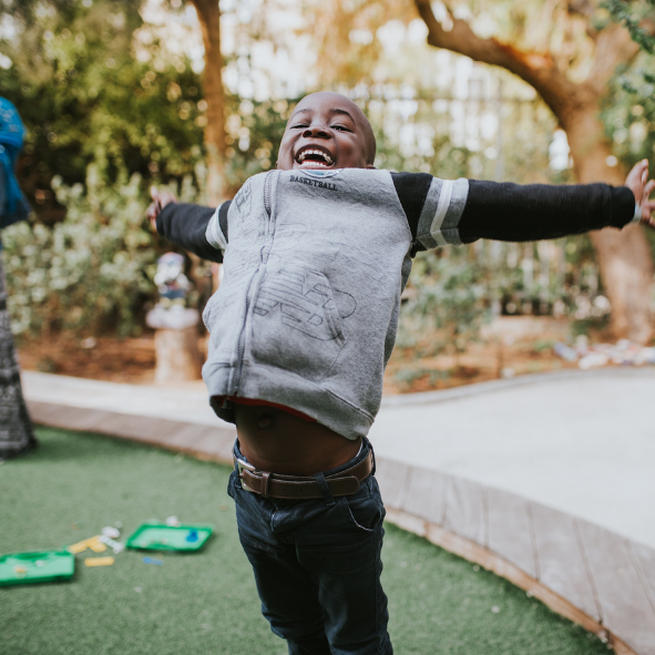 A Black boy in a gray hoodie with navy sleeves jumping.